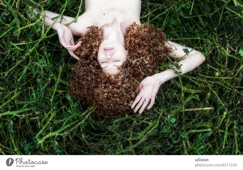 portrait of sexy young woman lying in tomato plants after harvest, with many hortensia flowers around the head instead of her hair, copy space. decorated crown