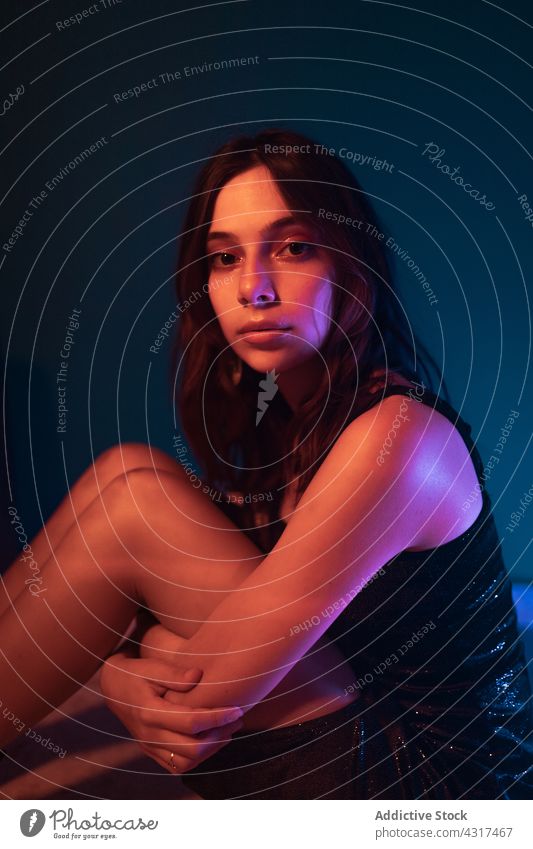 Young woman sitting in neon illumination light dark projector model style art fashion calm alone female young relax confident pensive appearance tranquil