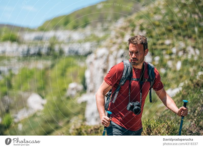 Male hiker walking with trekking poles in mountainous terrain tourist highland photo camera backpack rock tourism nature traveler adventure explore stick