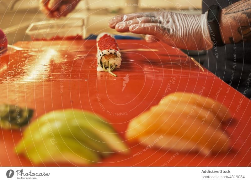 Crop chef preparing sushi at table in restaurant man cook roll kitchen asian food prepare seafood male cuisine rice salmon fish tobiko caviar ingredient