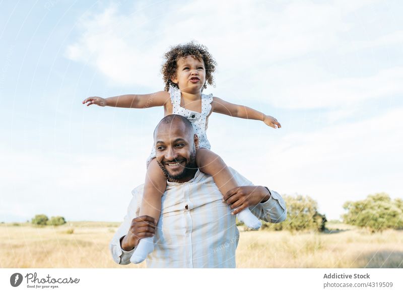 Delighted black father and daughter having fun in summer field on shoulders play ride together child playful game african american ethnic happy kid cheerful