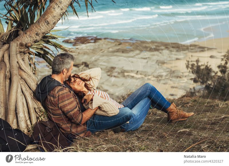 Middle-aged couple sitting under the tree, hug and look at each other. middle-aged woman ocean happy together palm park leisure love adult pretty relationship