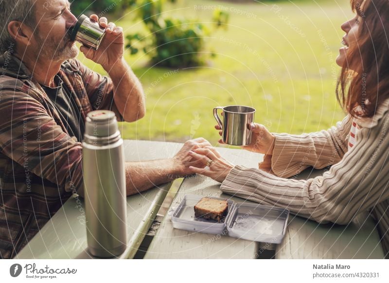 Middle-aged couple sitting on the benches with table in park and drinking tea. middle-aged woman happy ocean together leisure love adult pretty relationship