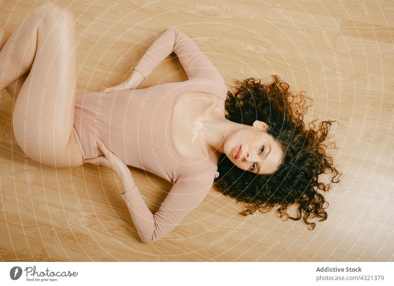 Graceful woman in bodysuit on floor grace studio tender style beige pastel color outfit female curly hair slender gentle slim feminine calm lying wooden parquet