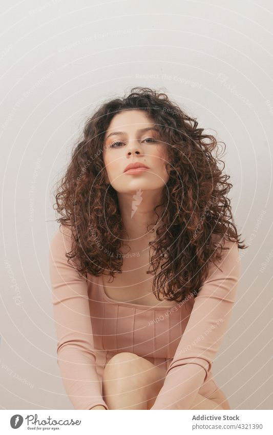 Delicate woman in beige bodysuit in studio tender grace pastel color charming gentle female style outfit curly hair slender sit floor slim feminine calm