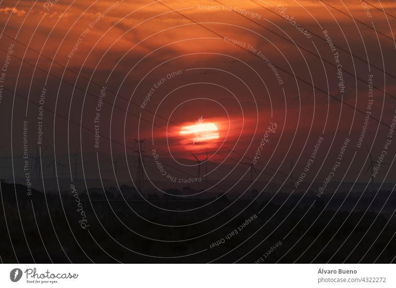 A huge red sun sets behind the clouds and a landscape of cables and wind turbines in the Ebro valley, near the town of Gallur, Aragon, Spain sunset giant