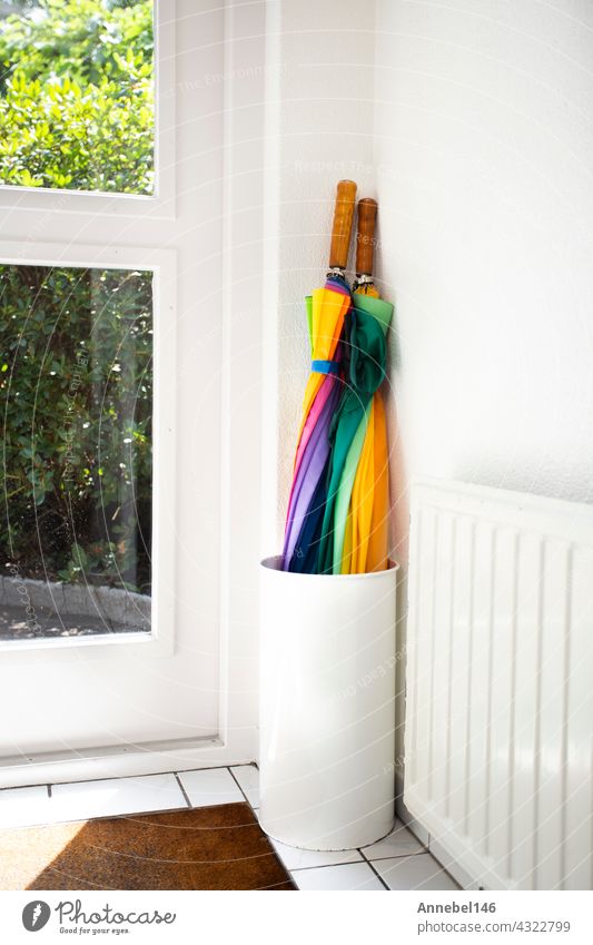 Umbrella in holder rainbow colored in white hallway, modern design in bright house next to door colorful umbrella background nobody apartment interior foyer