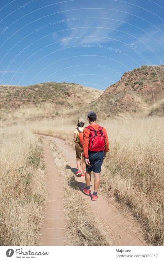 Caucasian couple 40-50, seen from their back, hiking in the nature in summer. El Cerro park, Alcala de Henares, Madrid, Spain, Europe cap shorts backpack