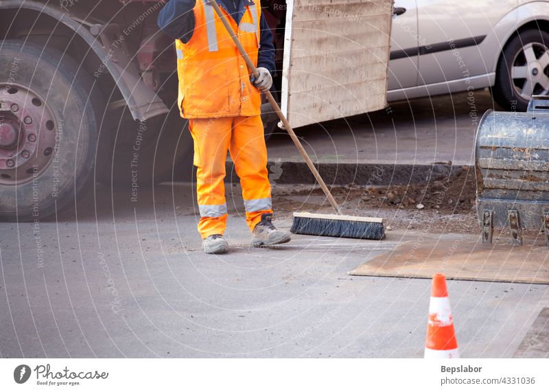 Worker in the street body brush brushing closeup construction details evening flattening holding implement industry legs leveling lower manual one orange