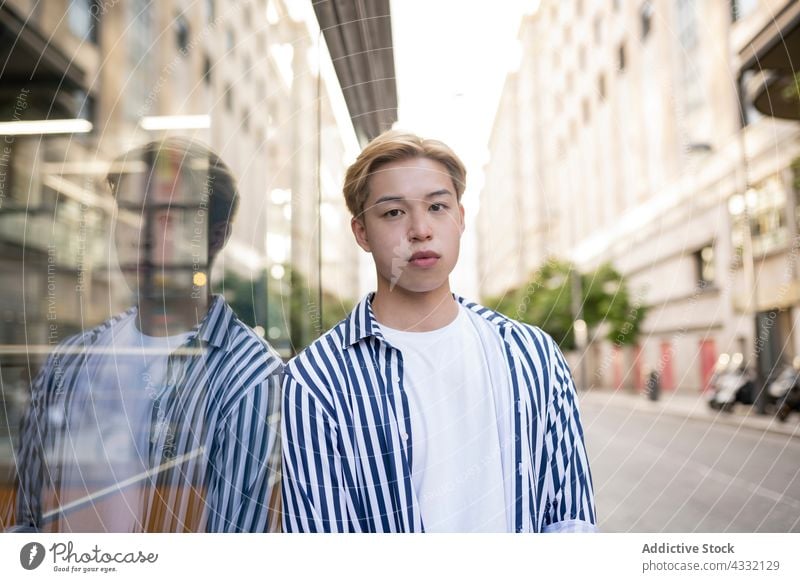 Asian man standing near glass wall in city model reflection mirror street style confident male ethnic asian fashion outfit urban blond trendy building lean