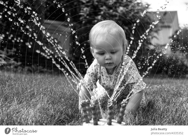 13 month old baby crawls up to a water sprinkler to play toddler sun safety water play yard home neighborhood midwest spf upf sun block clothing sunhat swimsuit