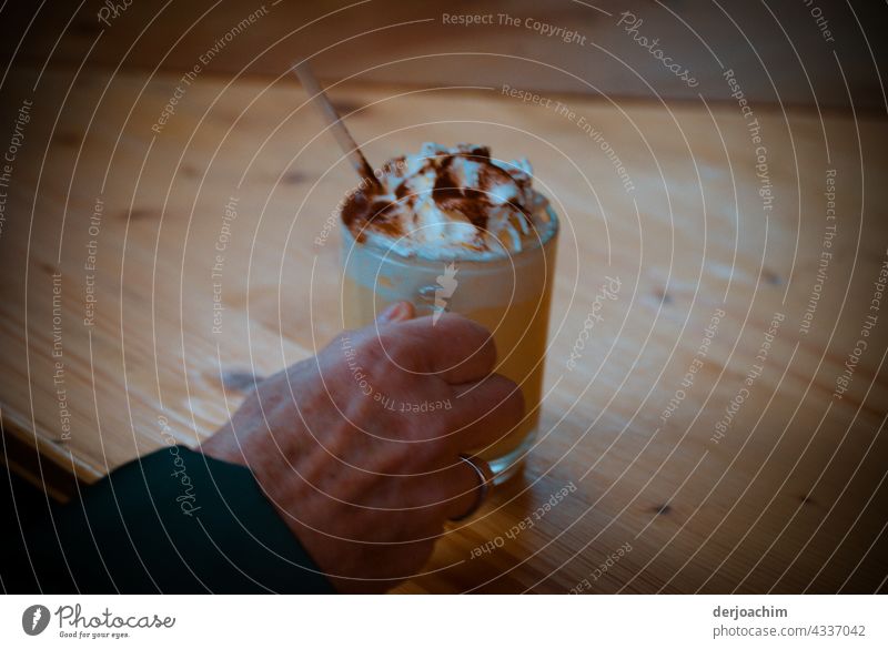 A refreshing drink is served, with cream and chocolate powder, over a wooden table. There is also a straw for the rest in the glass. Drinking Glass Beverage