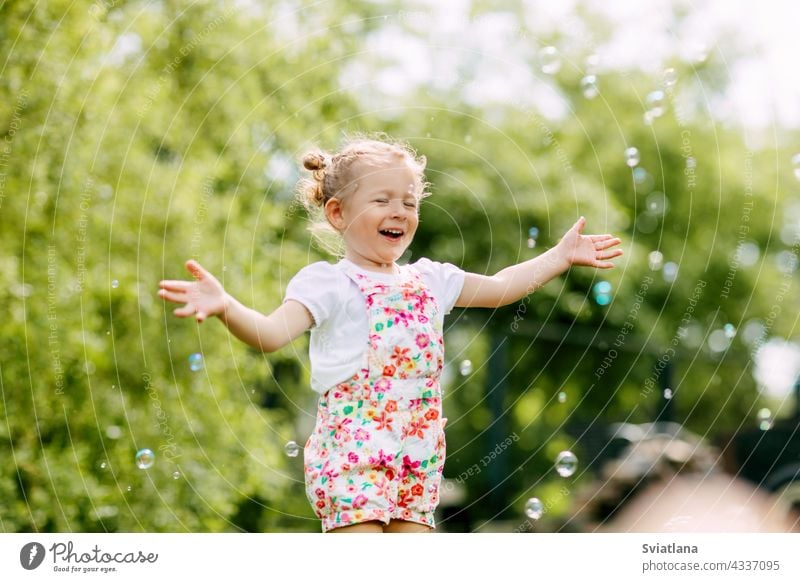 A cheerful girl catches soap bubbles with her hands and laughs. Happy childhood, summer time little joy baby green fun portrait blow beautiful kid park play