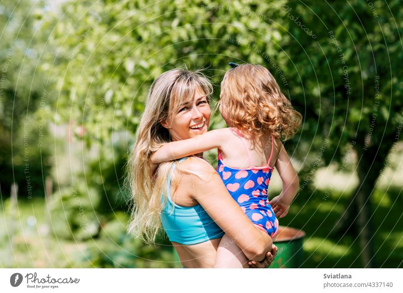 A young mother holds her little daughter in her arms on a summer day in the garden or park family parent mom child childhood happy togetherness motherhood care