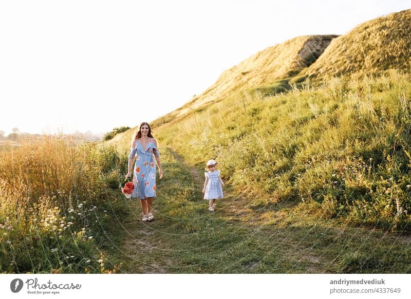 Young mother walking with her little daughter in the green field. Family holiday in garden. Portrait mom with child together on nature. Mum, little daughter outdoors. Happy Mothers Day. Close up.