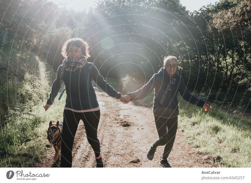 Senior woman and her daughter smiling and having fun on the forest during a sunny day. Running together with their dog, Happy mother's day joy laughing