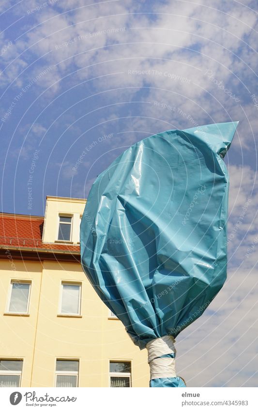 traffic sign covered with a blue plastic bag in front of an apartment house in the sunshine with deco clouds / construction site / invalid traffic sign