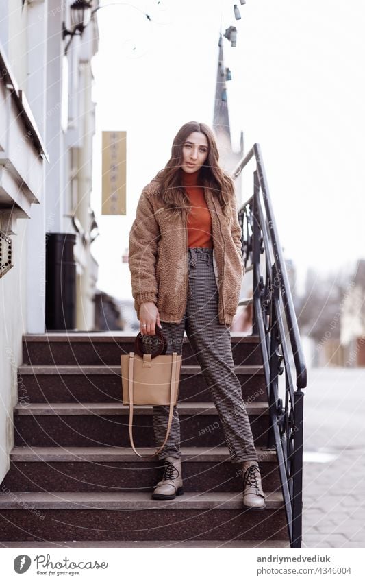 Fashion style portrait. beautiful stylish girl with long hair walks in the city. Portrait of attractive girl on the street. Spring or fall day. selective focus.