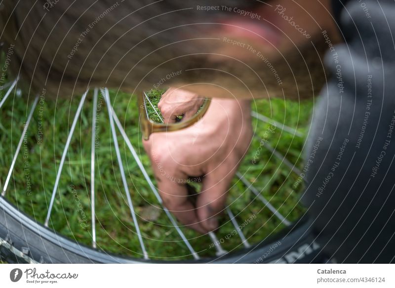 Young man checks the valve of his bicycle tire hands Handcrafts Air pump Bicycle Bicycle tyre Spokes Wheel rim Boots jeans Grass Plant Day daylight Close-up