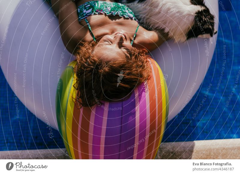 beautiful caucasian woman sitting on inflatable unicorn toy in swimming pool. Cute border collie dog besides. Summer time, vacation and lifestyle summer