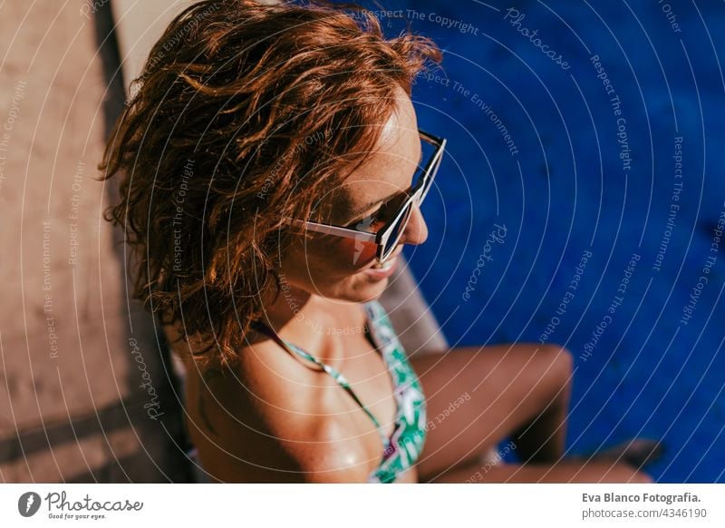 portrait of beautiful caucasian woman sitting by pool side wearing bikini swimwear. Summer time, vacation and lifestyle swimming pool sunglasses summer hot