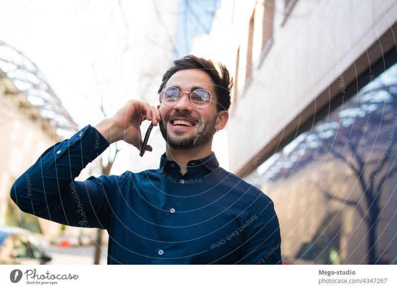 Young man talking on the phone outdoors. young mobile urban smiling smile connection gadget portrait positive wireless telephone holding walking looking typing