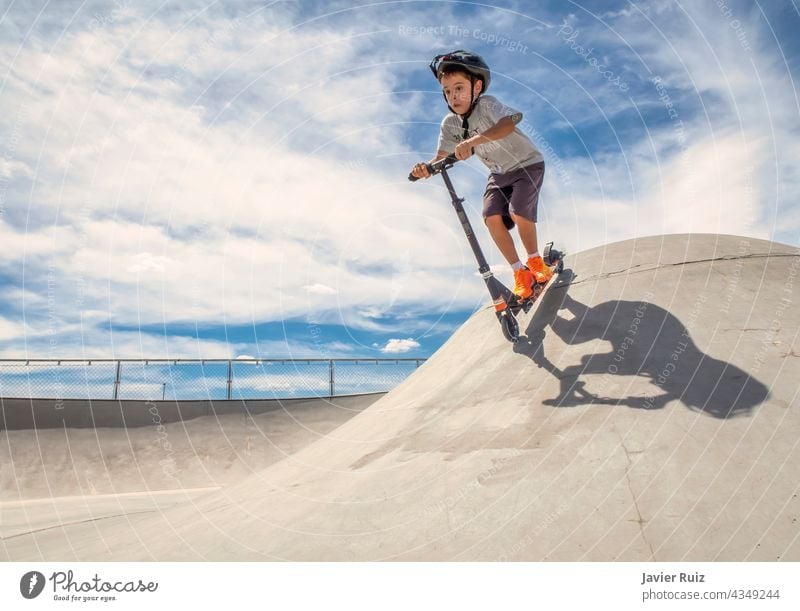 Child wearing a helmet goes down a ramp with a scooter in a skate park on a sunny summer day skater child boy skatepark funny playing speed lifestyle