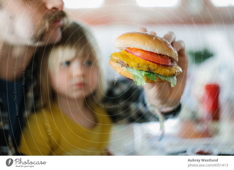 father and daughter eating a cheeseburger meal with fries in an american diner background barbecue bbq beef big blonde bread bun cheddar close up daddy date