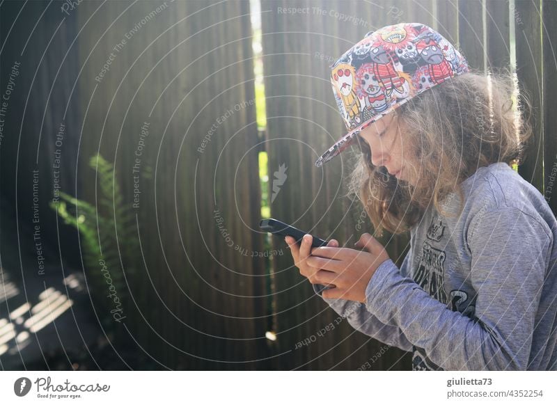 Teenage boy with cool baseball cap, online, outside engrossed in his mobile phone portrait Downward Central perspective Shallow depth of field Back-light