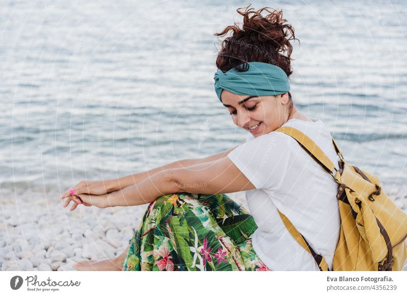 relaxed caucasian woman sitting by the beach during sunset. Wearing yellow backpack.summer time. daydreaming. Outdoors lifestyle ocean sea holidays vacation