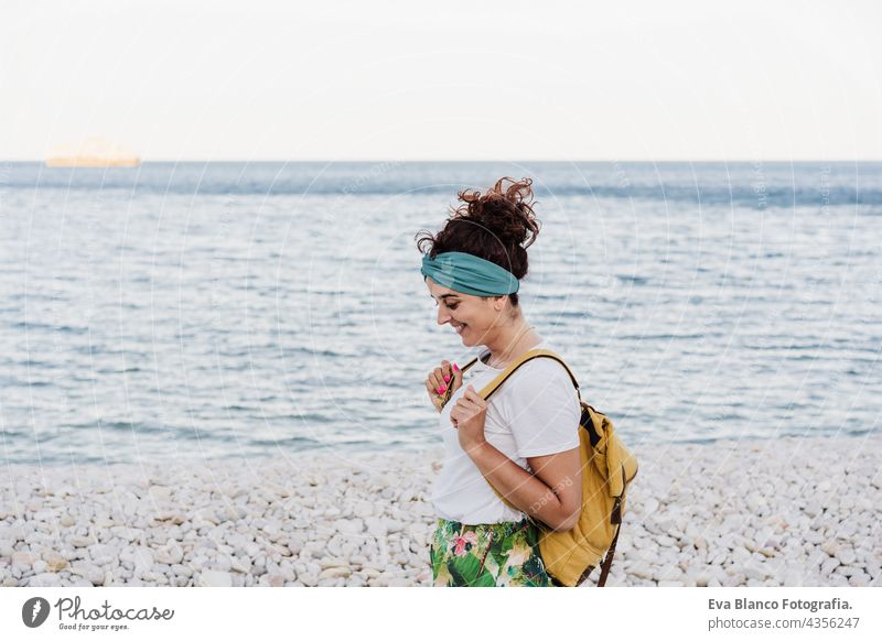 relaxed caucasian woman with yellow backpack walking by the beach during sunset. summer time. daydreaming. Outdoors lifestyle ocean sea holidays vacation