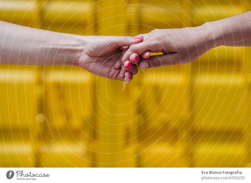 close up of lesbian couple holding hands in front of yellow background. Love is love . LGBTI concept unrecognizable happy caucasian women friends together