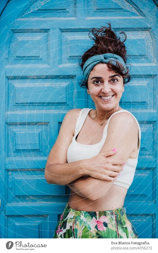 portrait of happy caucasian woman sitting in front of blue door during summer time. Outdoors lifestyle outdoors city beach carefree smiling smile town alicante