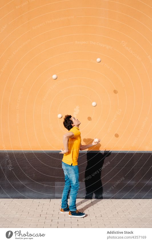 Agile man juggling balls near colorful wall juggle trick perform urban talent skill entertain male art activity practice stunt amusement motion exercise bright