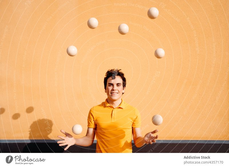 Agile man juggling balls near colorful wall juggle trick smile perform urban talent skill happy entertain male art activity practice stunt amusement motion