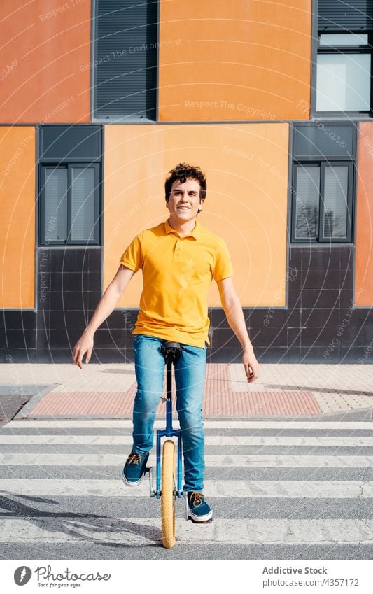 Young man on unicycle on city street crosswalk ride urban color modern orange asphalt road style balance wheel zebra male crossing lifestyle vehicle transport