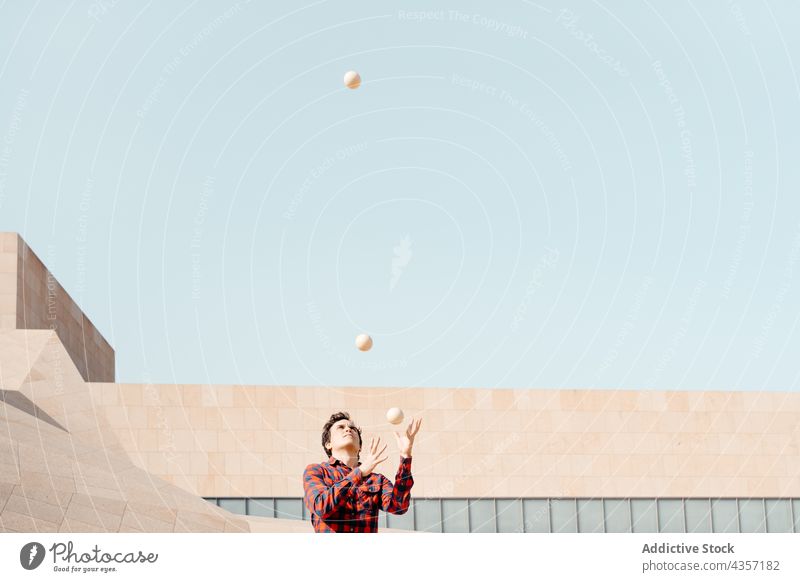 Young man juggling balls near modern building juggle trick perform architecture contemporary geometry entertain talent art skill activity practice male young