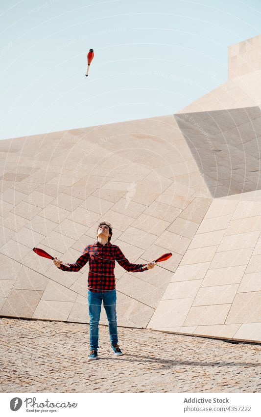 Man juggling clubs near geometric building man juggle trick perform architecture contemporary geometry entertain talent art skill activity practice male modern