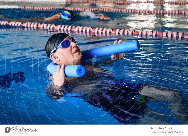 Mature man swimming on aqua noodle in pool water aerobic exercise mature training male activity sport swimwear healthy relax rest active recreation wellness