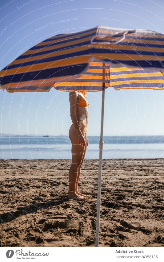 Anonymous woman standing on beach bikini fit summer vacation beach umbrella sea travel holiday pale anonymous young redhead slim orange female water chair sand