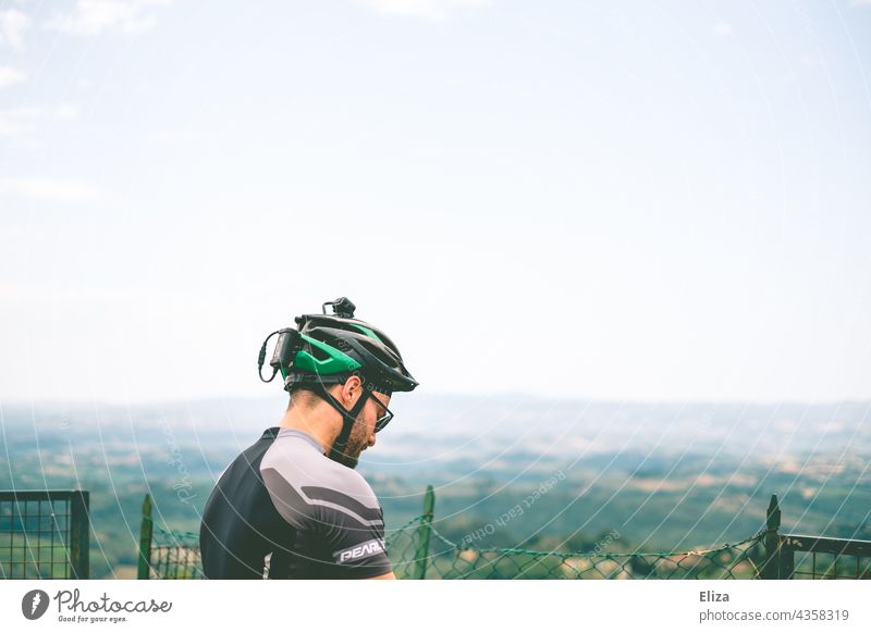 Man in cycling clothes with bicycle helmet in front of a view of the countryside Bike helmet Bicycle clothing Sportswear Cycling tour Landscape Vantage point