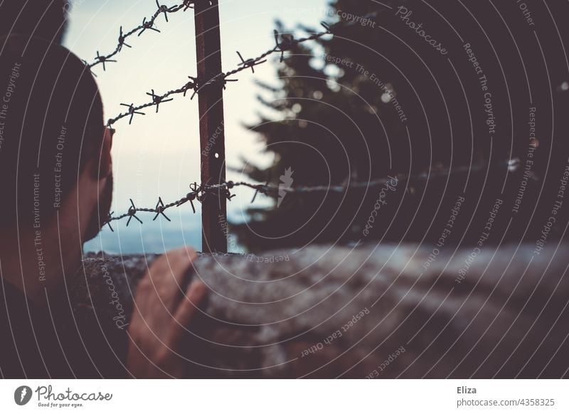 Man looking over a fence with barbed wire. Concept of being trapped and wanderlust. Barbed wire Captured Fence jail Barbed wire fence Border Barrier Safety