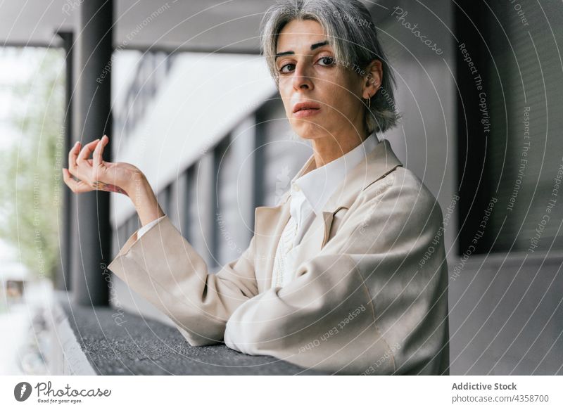 Transgender woman standing near fence in city street transgender trendy style lgbt urban determine female self confident queer identity lean coat fashion modern