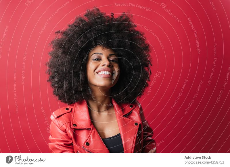 Cheerful black woman with curly hair looking at camera on red background afro hairstyle cheerful appearance smile color charming female ethnic african american