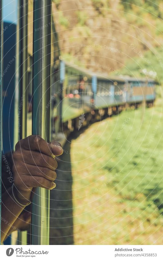 Crop unrecognizable ethnic man riding train and looking out of wagon travel ride passenger traveler window scenery journey male freedom recreation transport