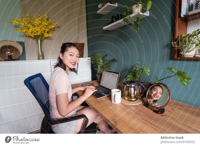 Delighted Asian woman reading document on laptop and working at home freelance smile computer female asian delight ethnic netbook job happy cup online using