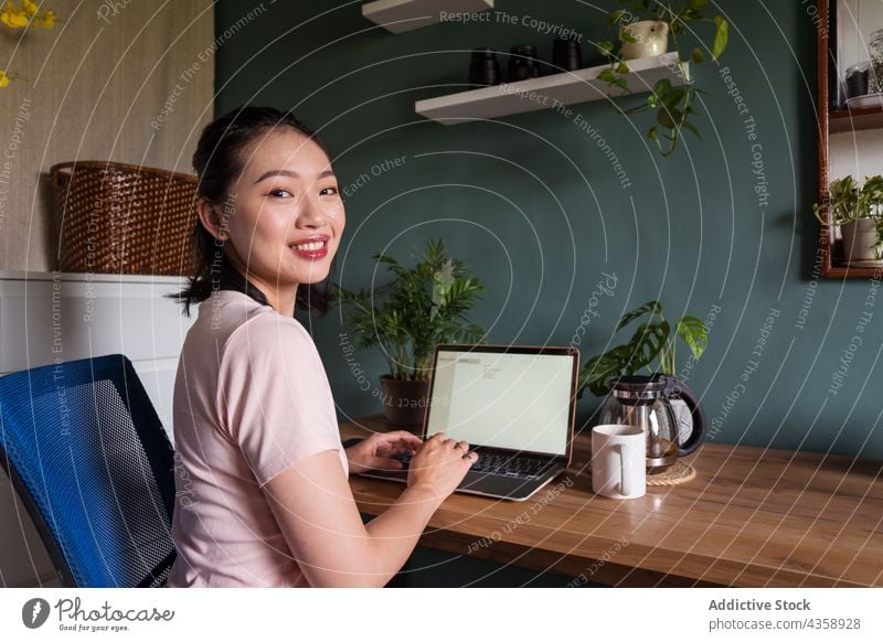 Delighted Asian woman reading document on laptop and working at home freelance smile computer female asian delight ethnic netbook job happy cup online using