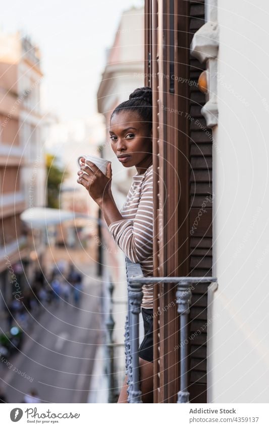 Black woman with coffee contemplating town from balcony reflective wistful hot drink thoughtful lonely house contemplate alone african american black ethnic