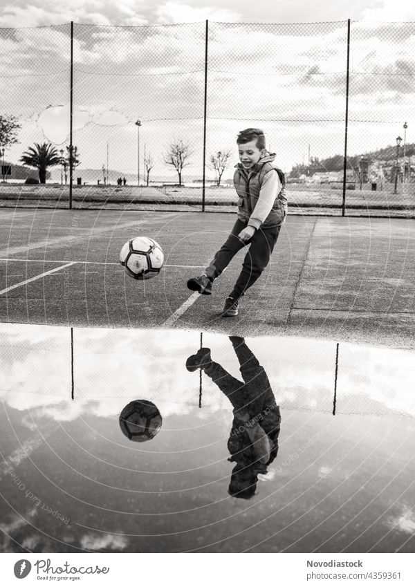 young boy kicking a ball on black and white kid child one 1 youth football soccer outdoors outside park pavement leg round sport active lifestyle healthy speed