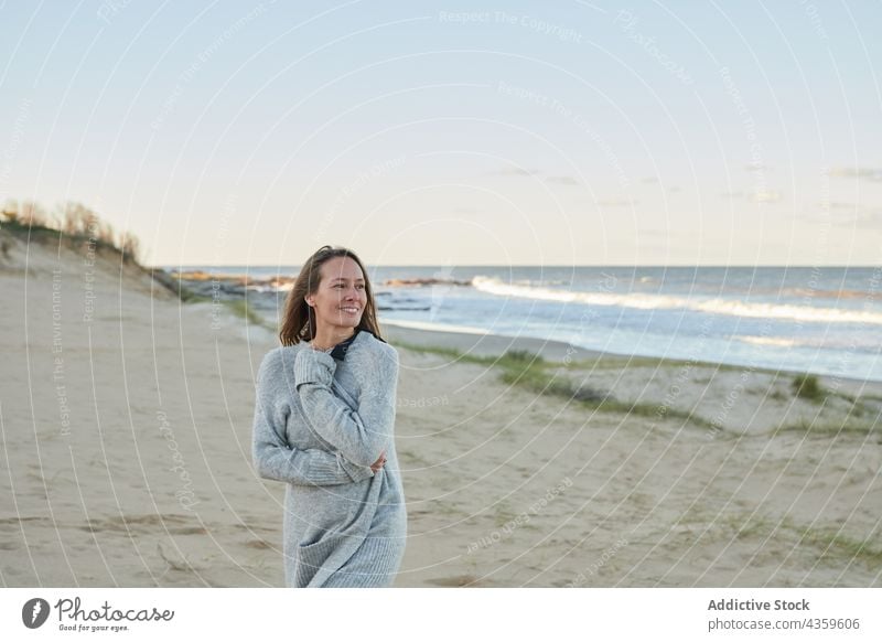 Smiling woman standing on sandy seashore in summer beach enjoy sunset evening smile vacation female coast seaside water content carefree ocean travel cheerful